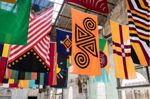 Archie Moore, United Neytions (2014–2017). Installation of 28 flags, polyester, nylon, zinc plated alloy. 28 parts in two sizes: 23 x 360 x 180 cm and 5x 180 x 180 cm. Exhibition view: The National: New Australian Art, Carriage works, Sydney (2017). Courtesy the artist and The Commercial. Sydney. Photo: Sofia Freeman.